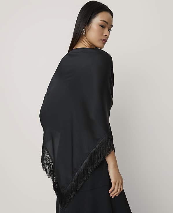 A woman wearing a black fringed shawl stands against a plain, light-colored background.