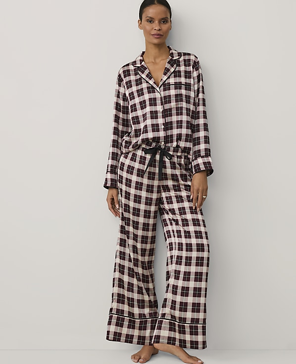 A woman wearing burgundy and white checkered pajamas stands against a plain white background.