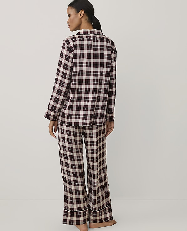 A woman stands with her back to the camera wearing burgundy and white plaid pajamas against a plain white background.