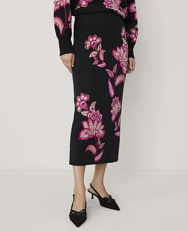 A person wears a black floral knit skirt and matching top with black pointed-toe heels against a plain white background.