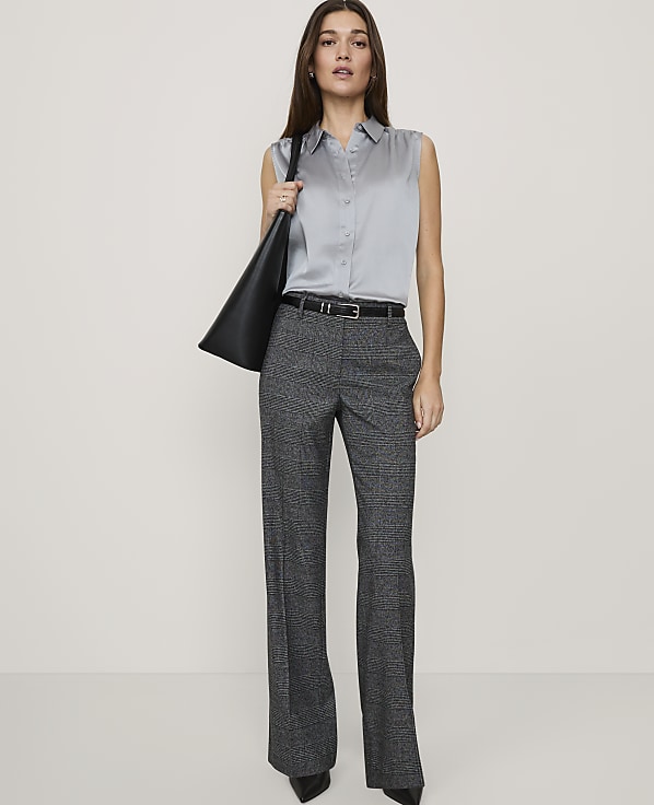 A woman wearing a sleeveless grey shirt and wide-leg patterned trousers stands against a plain white background.