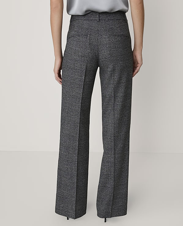 A person wears grey plaid wide-leg trousers and a silver top against a plain, light-colored background.