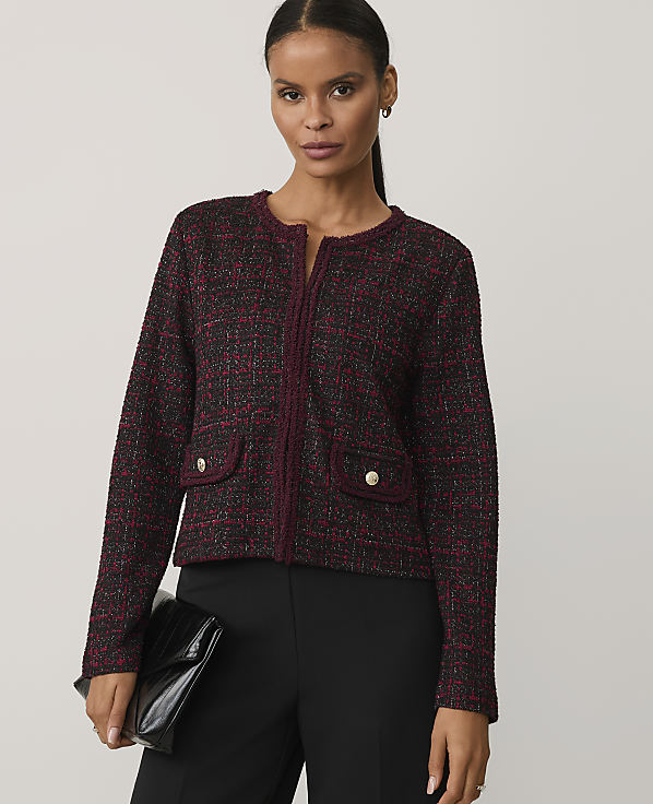 A woman wearing a burgundy tweed jacket and black trousers stands against a plain light gray background.