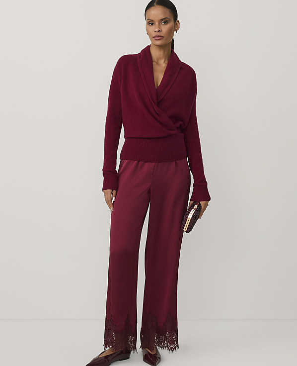 A woman wearing a burgundy wrap sweater and matching satin trousers with lace hems stands against a plain white background.