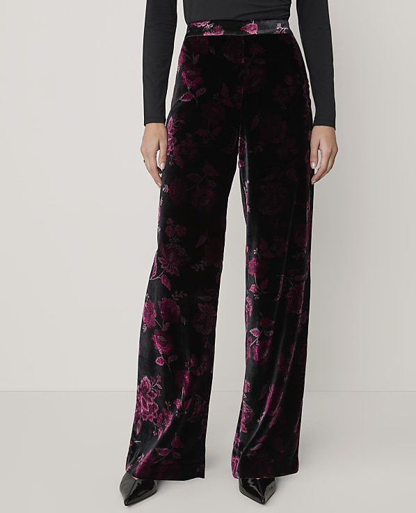 A person wears wide-leg black and purple floral velvet trousers and a black top against a plain light grey background.