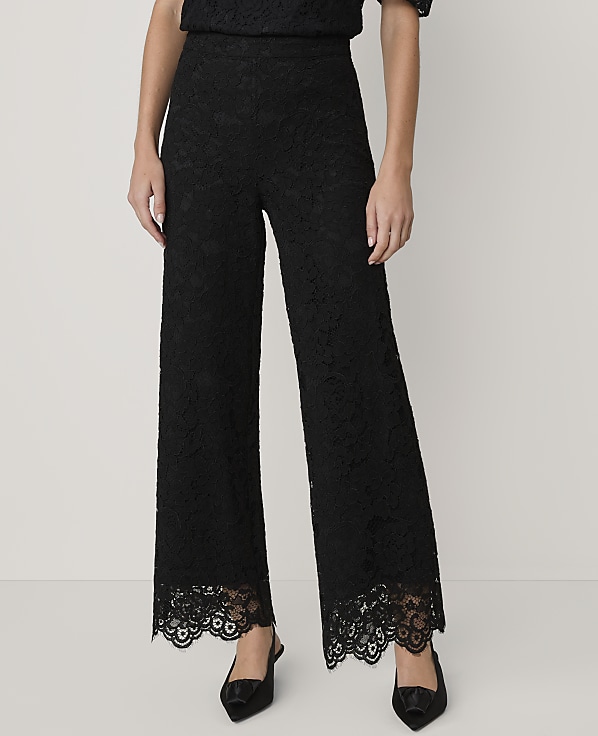 A person wears black lace wide-leg trousers and pointed heels against a plain light grey background.