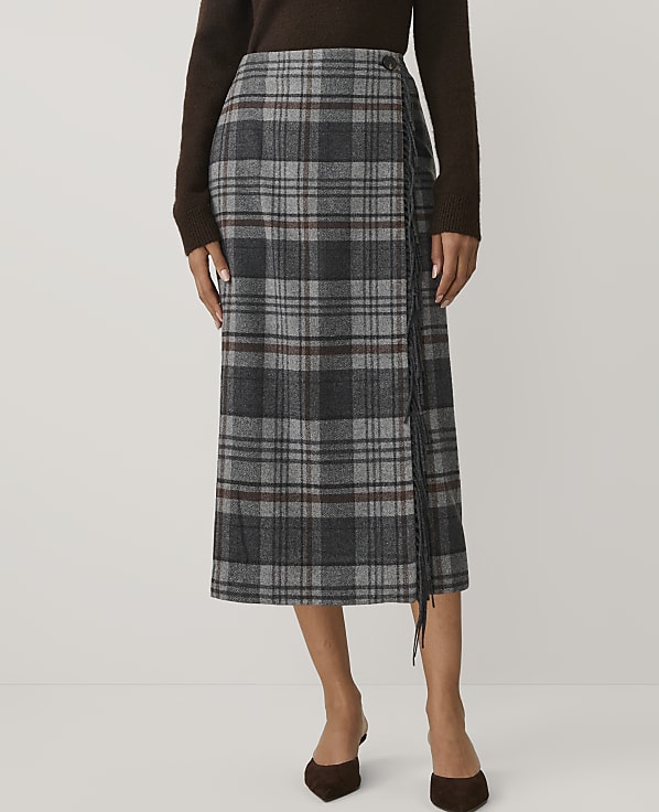 A person wears a grey plaid midi skirt and a brown sweater against a plain white background.