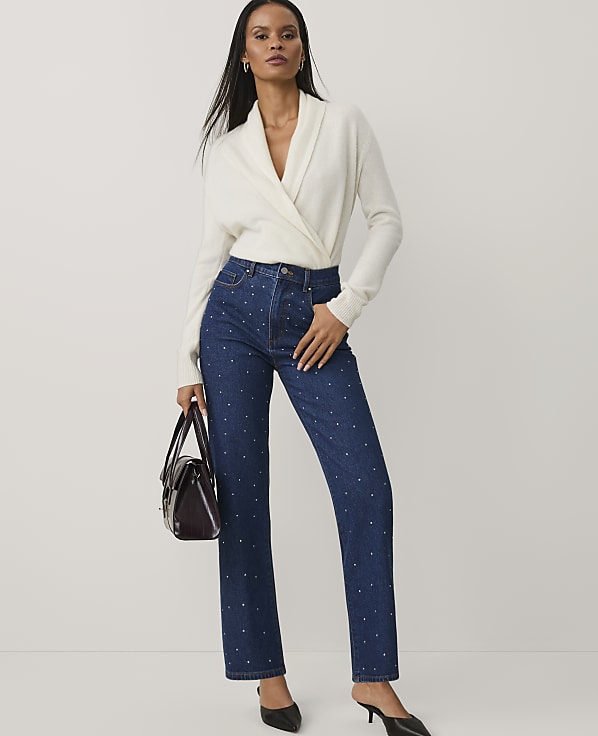 A woman wearing a white wrap sweater and blue star-patterned jeans stands against a plain light gray background.