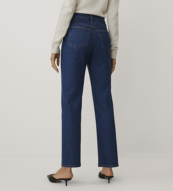 A person wearing a white sweater, blue jeans, and black mules stands against a plain white background.