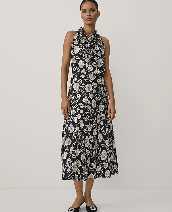 A woman wearing a black and white floral print dress and black heels stands against a plain white background.