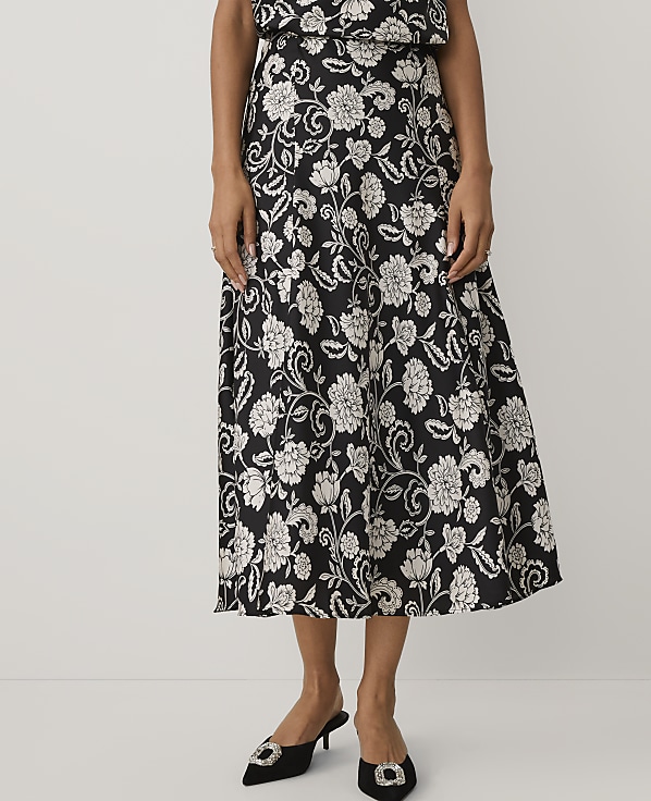 A person wears a black and white floral print midi dress and black pointed-toe heels against a plain white background.