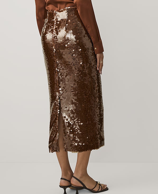 A person wears a shimmering bronze sequined midi skirt and a brown top against a plain white background.