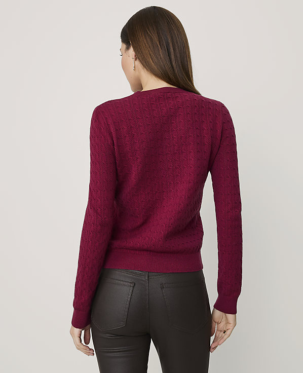 A woman wearing a textured magenta sweater and dark brown leather pants stands against a plain light gray background.