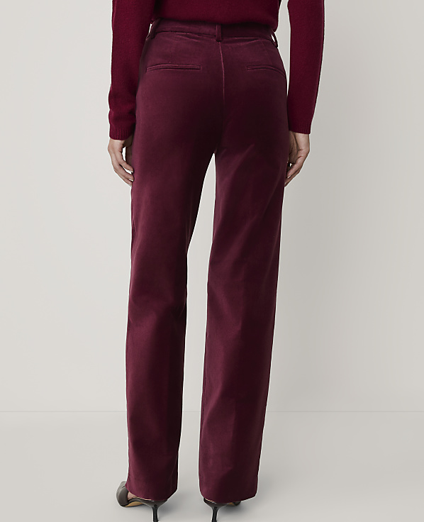 A person wearing a burgundy sweater and matching velvet trousers stands against a plain, light-colored background.