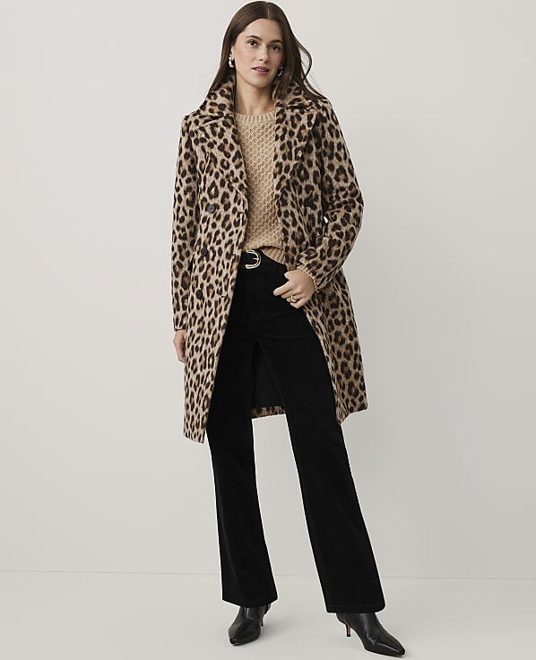 A woman wearing a leopard print coat, beige sweater, and black flared trousers stands against a plain white background.