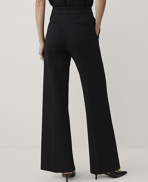 A person wearing wide-leg black trousers and black heels stands against a plain, light-colored background.