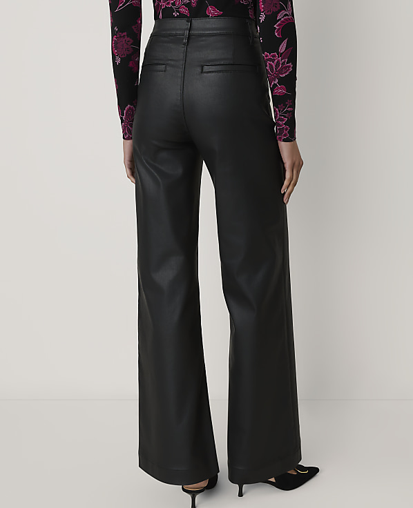 A person wearing black leather wide-leg trousers and a floral top stands against a plain white background.