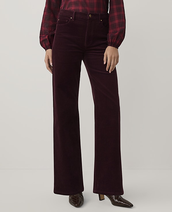 A person wearing a red plaid shirt and burgundy corduroy wide-leg trousers stands against a plain light gray background.
