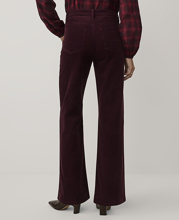 A person wearing a red plaid shirt and burgundy corduroy flare pants stands against a plain white background.