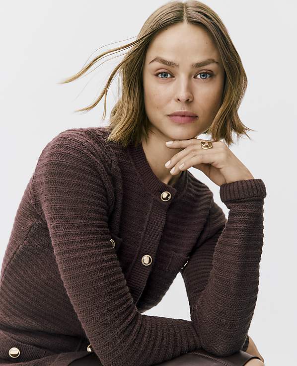 A woman with blonde hair wearing a textured burgundy cardigan poses against a plain white background.