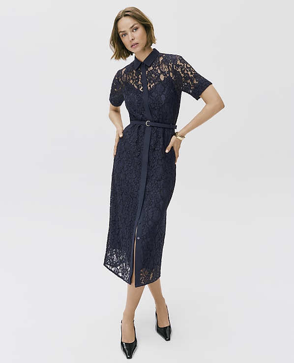 A woman wearing a navy blue lace midi dress and black heels stands against a plain white background.