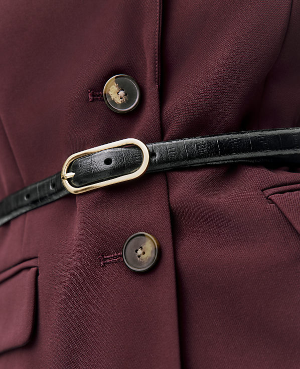 A black leather belt with a gold buckle is fastened across a maroon blazer featuring two brown buttons.