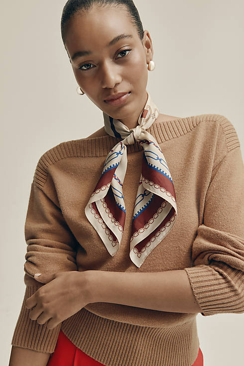 A woman wearing a tan sweater and a patterned silk scarf poses against a plain, light-colored background.