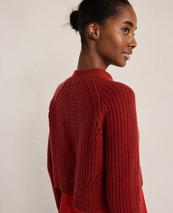 A woman with her hair in a bun wears a red knit sweater against a plain, light-colored background.