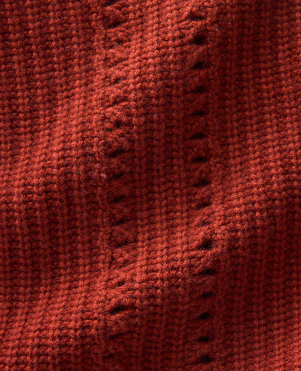 A close-up of textured red knitted fabric with vertical ribbed patterns in the foreground and soft folds in the background.