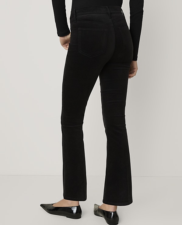 A person wearing black flared trousers and black flats stands against a plain white background.
