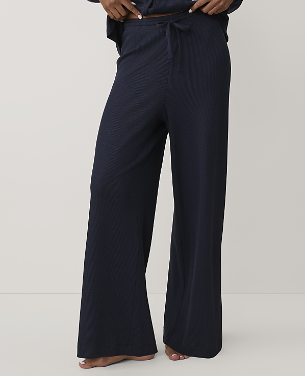 A person wears navy blue wide-leg ribbed trousers against a plain, light-colored background.