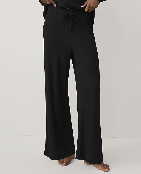A person wears black ribbed wide-leg lounge pants against a plain, light-colored background.