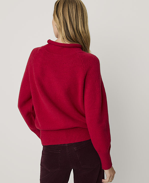A woman wearing a bright red sweater and dark burgundy corduroy pants stands against a plain white background.