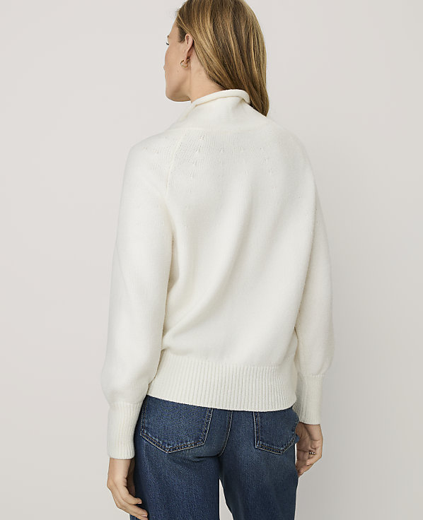 A woman wearing a white fuzzy sweater and blue jeans stands with her back to the camera against a plain light gray background.