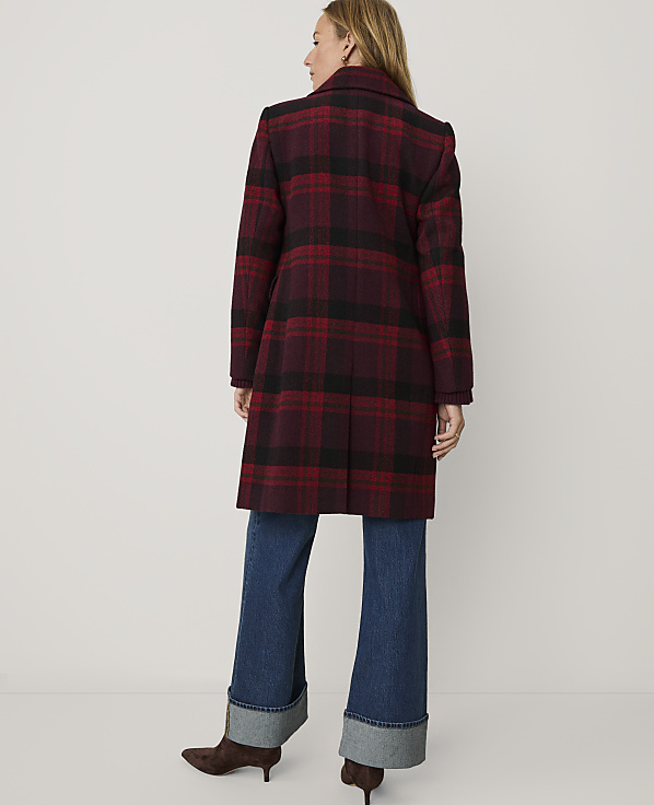 A woman stands with her back to the camera wearing a red and black plaid coat and wide-leg blue jeans against a plain white background.