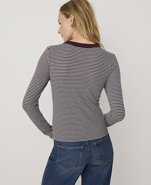 A woman wearing a maroon and white checkered long-sleeve shirt and blue jeans stands against a plain white background.