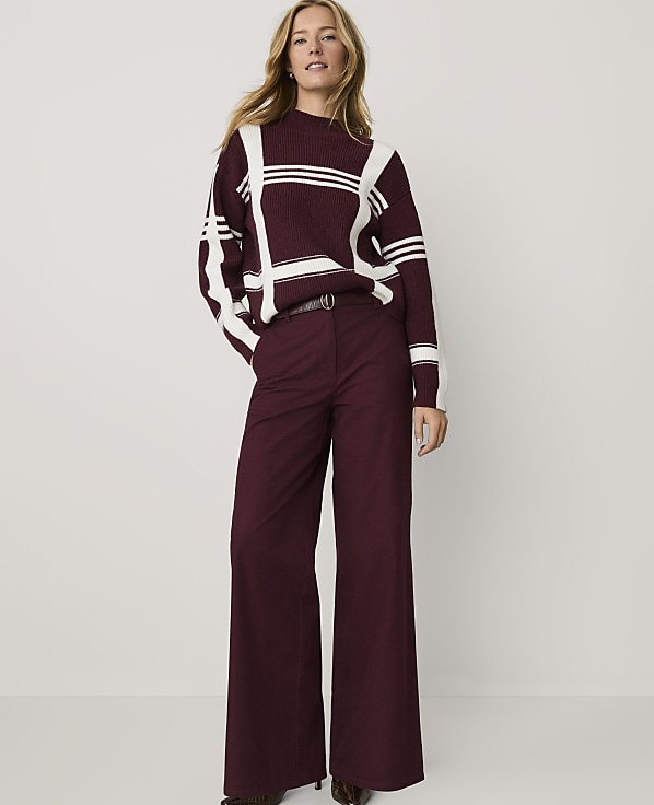 A woman wearing a maroon and white striped sweater and matching wide-leg trousers stands against a plain white background.