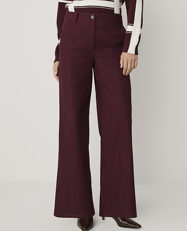 A person wears wide-leg burgundy trousers and a striped sweater against a plain, light-colored background.