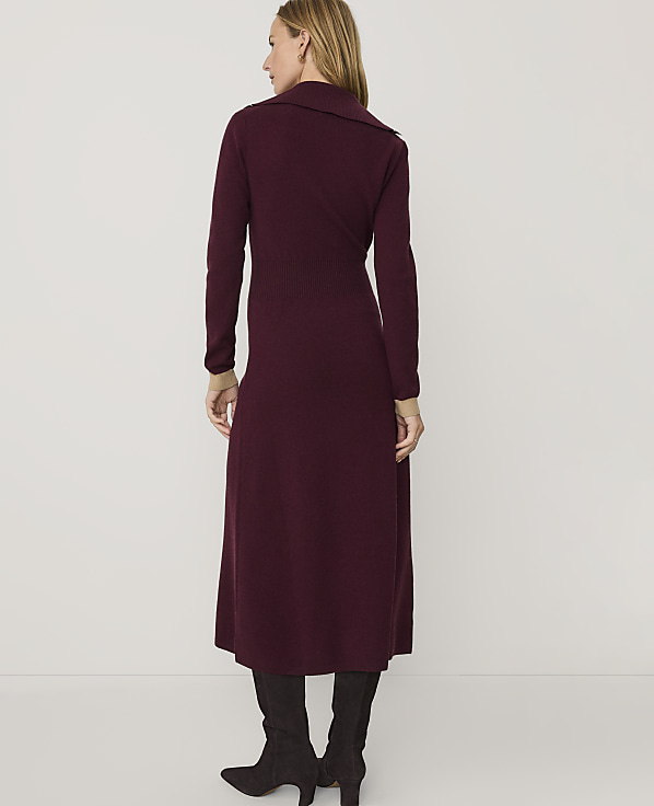 A woman wearing a long, burgundy knit dress and dark grey boots stands against a plain white background.