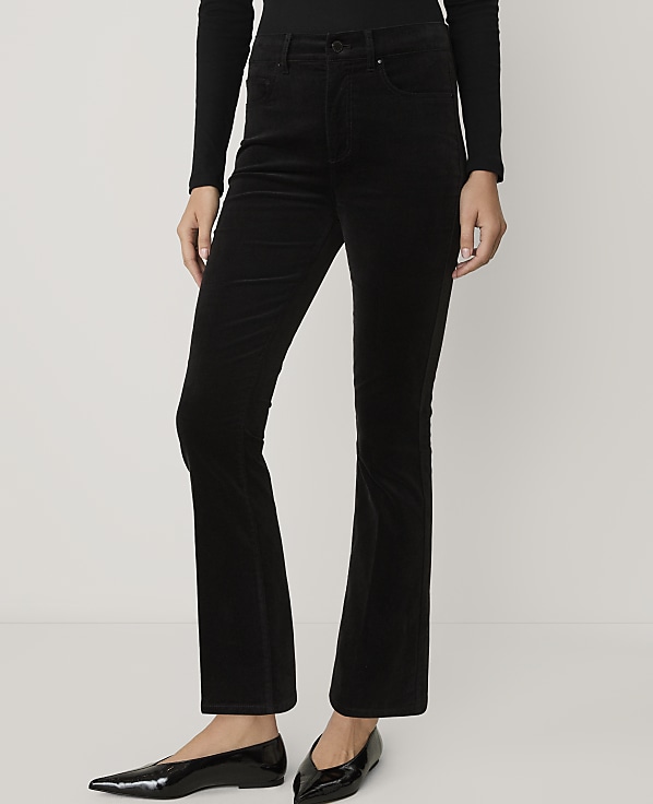 A person wearing a black long-sleeved shirt, black flared corduroy trousers, and black pointed-toe flats stands against a plain white background.