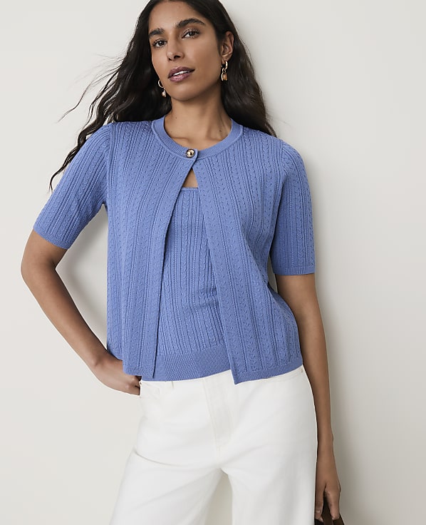 A woman in a blue cardigan and matching top stands against a plain, light-colored background.