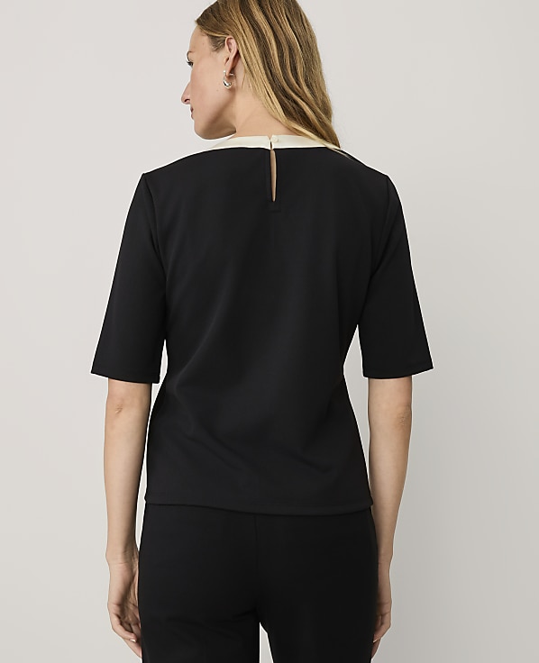 A woman wearing a black short-sleeved top and black pants stands with her back to the camera against a plain light gray background.