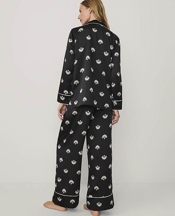 A woman stands with her back to the camera wearing black floral pajamas against a plain white background.