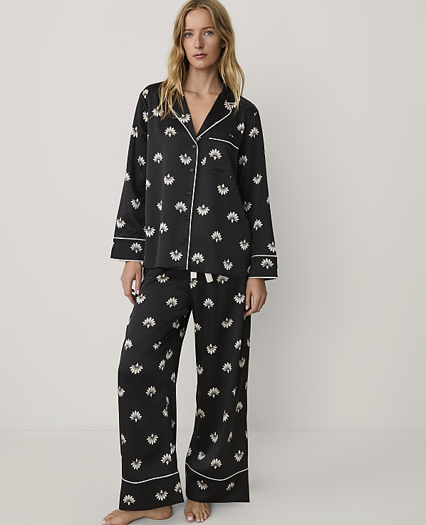 A woman wearing black floral pajamas stands against a plain, light-colored background.