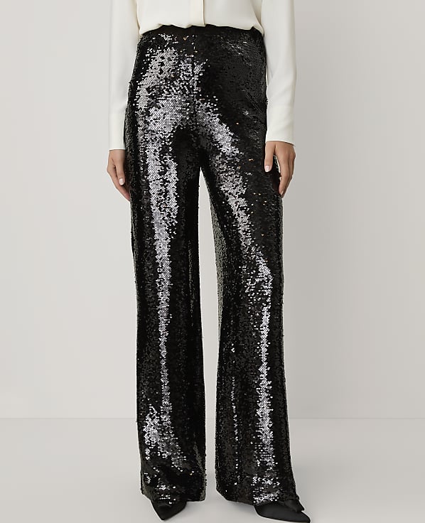 A person wears shimmering black sequined wide-leg trousers and a white top against a plain, light-colored background.