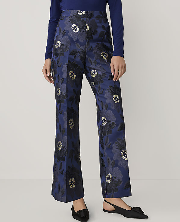 A person wears a blue long-sleeved top and blue floral-patterned wide-leg trousers with black pointed-toe flats against a plain white background.