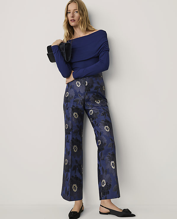 A woman wearing a blue off-the-shoulder top and floral patterned blue trousers stands against a plain white background.