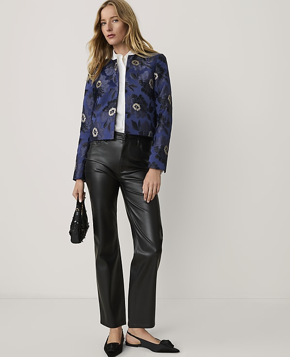 A woman wearing a blue floral jacket and black leather trousers stands against a plain white background.