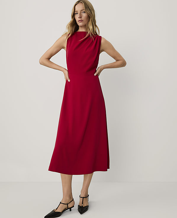 A woman wearing a sleeveless red midi dress and black pointed-toe heels stands against a plain, light-colored background.