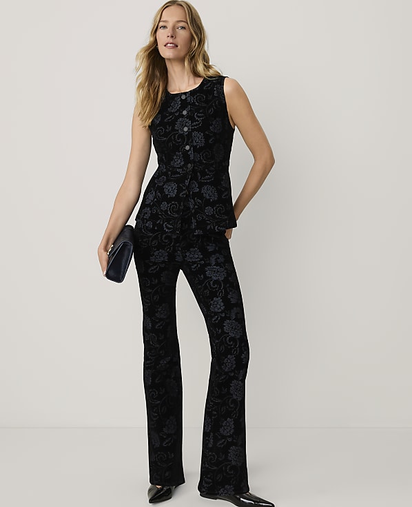 A woman wearing a black floral patterned sleeveless top and matching trousers stands against a plain white background.
